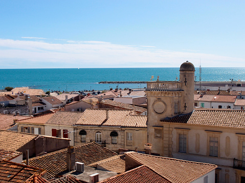 Aerial view of the old coastal town. View of the roofs of the old coastal town. The view of the terracotta tiled roofs of the coastal town houses against the background of the calm sea and the blue cloudless sky. Saintes-Maries-de-la-Mer, Bouches-du-Rhône, France.