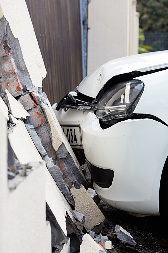 Cape Town, South Africa - August 11, 2022: The damaged front of a car and a cracked, leaning suburban boundary wall in the immediate aftermath of a collision in the Cape Town southern suburb of Plumstead.