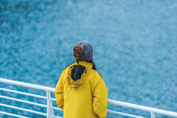 Woman in yellow jacket is standing on cruise ship and looking at view in Alaska. stock photo