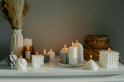 Home interior decor. White dresser with dried flowers in vase, rattan bags and candles. Still life, hygge concept