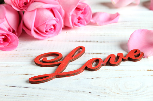 Pink roses and the word love on a white wooden background.