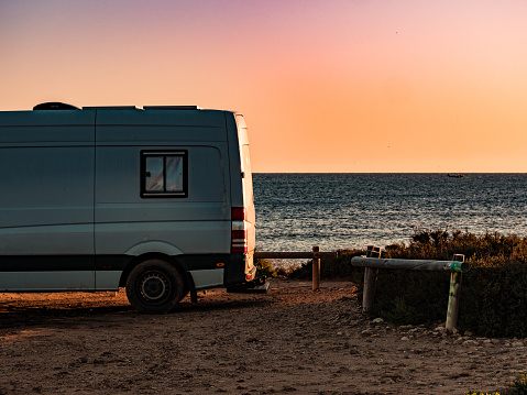 Camper recreational vehicle at sunrise on mediterranean coast in Spain. Camping on nature beach. Vacation and traveling in motor home.