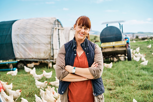 Farming and agriculture with a female farmer on a chicken, poultry or farm, smiling and standing with her arms crossed. Raising and breeding livestock on a sustainable, organic and free range ranch