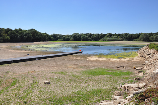 Low water in reservoir illustrates drought, heatwave and water shortages. Dry hot arid climate change. Outdoors on a summer day. Hanningfield Reservoir, Essex, United Kingdom, August 11, 2022