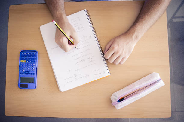 boy doing homework in class using calculator and pencil on a table stock photo