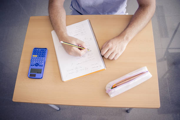 boy doing homework in class using calculator and pencil on a table stock photo
