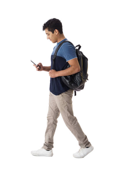 istock Latin male student walking and looking down at phone 1414245106