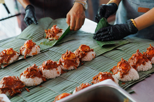 Nasi Lemak is coconut rice with toppings like fried anchovies, prawns roasted peanuts, hard boiled egg, fresh cucumber, and sambal. Sold as a street food snack wrapped in a banana leaf.