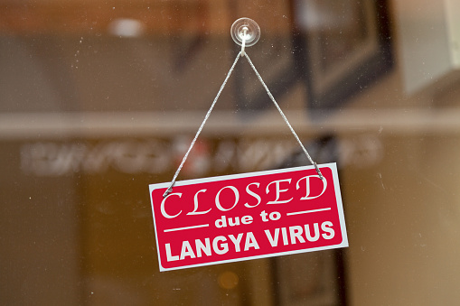 Red sign hanging at the glass door of a shop with written in it Closed due to Langya virus.