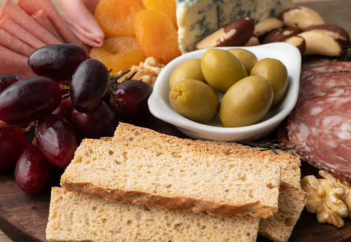 Appetizer board with cheese, nuts, fruits, toasts and charcuterie over wooden table.