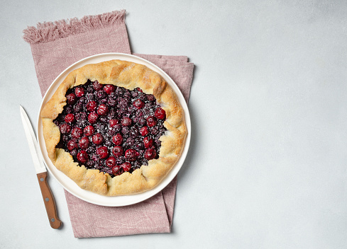 Fresh cherry and blueberry galette with coconut on white plate, top view, copy space. Homemade rustic dessert - american pie or tart or cake or french galette on a white background