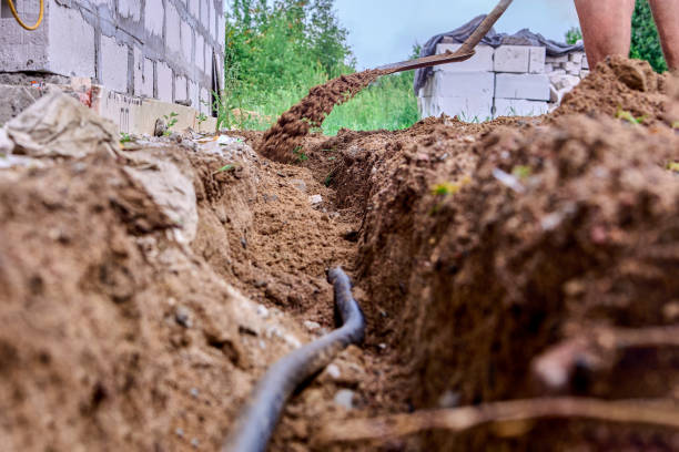 istock Construction worker is digging trench for laying cables, using shovel to excavate soil. 1414250816