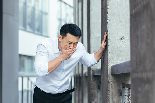 Sick businessman, Asian man has severe nausea outside near the office