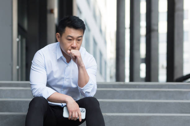 upset asian sitting on stairs outside office center, depressed man and frustrated businessman - men asia asian culture asian ethnicity imagens e fotografias de stock