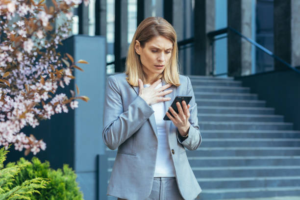 Frustrated and shocked business woman reading bad news online from phone Frustrated and shocked business woman reading bad news online from phone, businesswoman outside office in business suit email scam stock pictures, royalty-free photos & images
