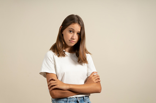 Portrait of angry hispanic teenage girl with arms crossed in warning gesture, isolated on beige studio background