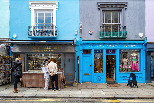 London, UK - 12 March 2022: Tourists browse in the colourful shops of Portobello Road, London. This district in Notting Hill is famous for numerous pastel painted terraces.