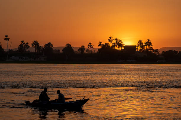Pyramids of Giza, Giza Necropolis, Egypt - July 26, 2022: Two men rowing a small boat during sunset on the Nile River.