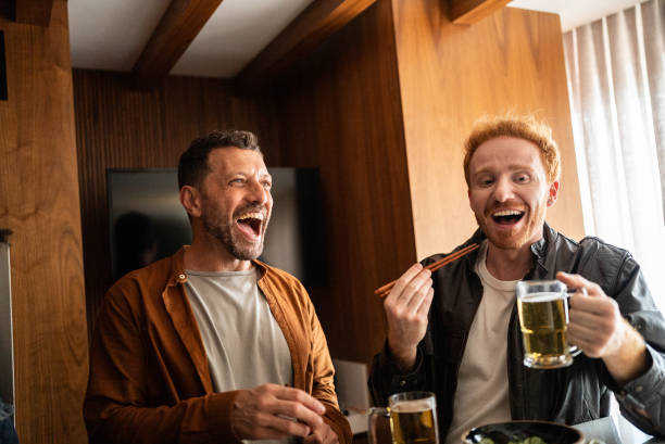 Friends talking and eating asian food at home Friends talking and eating at home two mature men enjoying a beer stock pictures, royalty-free photos & images