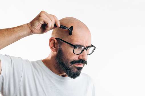 Concentrated man shaving his head. Bald person with glasses and shaver