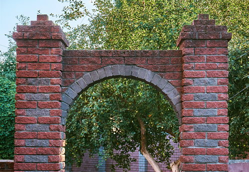 Brick arch of red stone, construction and decoration of the passage on the territory of the house or plot. Decorative structure in the form of an arc.