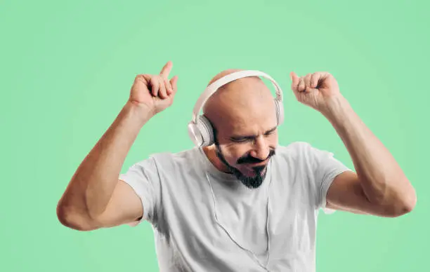 Photo of Bald man listening and enjoy the music and dancing on green background. Entertainment, sound, bass and mood