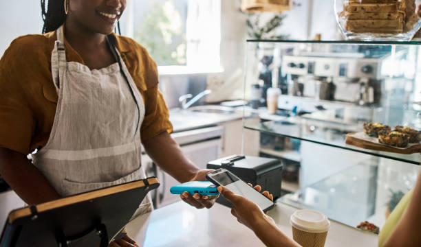 istock Cashier tapping customer phone on a machine for contactless and secure payment at a cafe store. Modern and trendy female small business owner using snap scan transaction to pay for service at a shop 1414263326