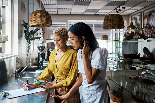 Small business owners working together and writing down orders in a coffee shop. Female entrepreneurs in partnership collaborating, brainstorming and planning sales for their cafe