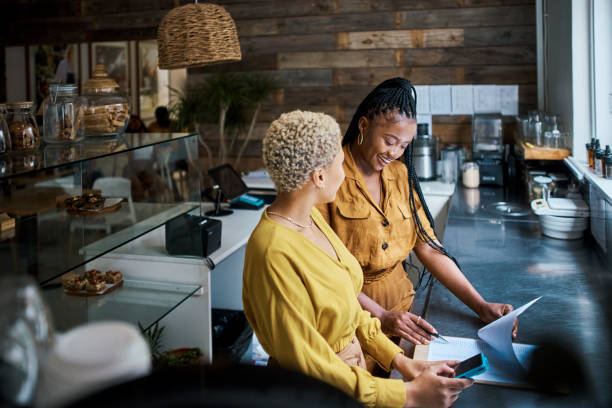 small business owner training new employee on the job at a coffee shop. black female entrepreneurs in a partnership collaborating and planning finance and growth together inside the cafe - family business stockfoto's en -beelden