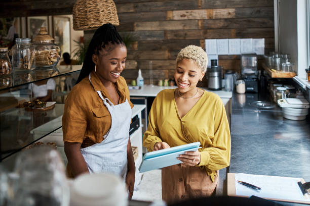 gerente de cafetería, propietario y supervisor usando una tableta para capacitar a una camarera en su tienda. trabajadores hablando mientras revisan pedidos en línea y usan una aplicación móvil para anuncios de redes sociales en un café - restaurant review fotografías e imágenes de stock