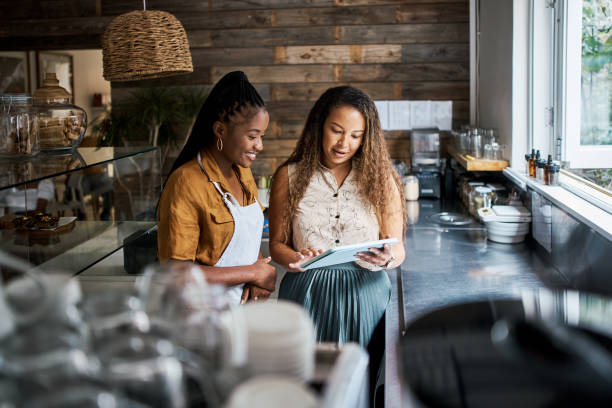 pracownica kawiarni planująca menu lunchowe na cały dzień z baristą w kuchni. nowoczesna praca pracowników restauracji szkolących nowych pracowników. młode kobiety pracujące zespołowo i uczące się obsługi detalicznej - job orders zdjęcia i obrazy z banku zdjęć