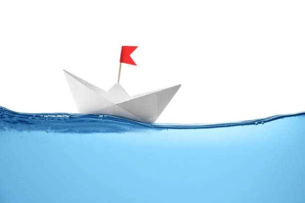 istock Handmade paper boat floating on clear water against white background 1414263588