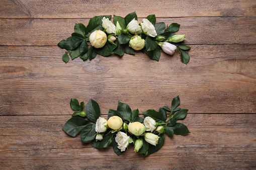 Wreath made of beautiful flowers and green leaves on wooden background, flat lay. Space for text