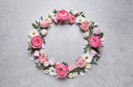 Wreath made of beautiful flowers and green leaves on light grey background, flat lay. Space for text