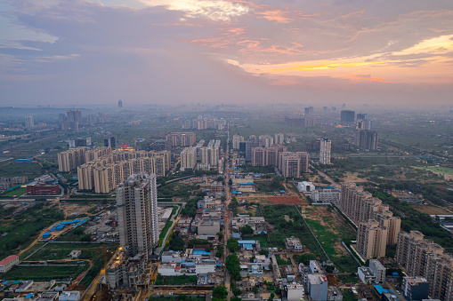 drone aerial shot showing busy traffic filled streets between skyscrapers filled with houses, homes and offices with a red sunset sky showing the hustle and bustle of life in Gurgaon, delhi drone shot