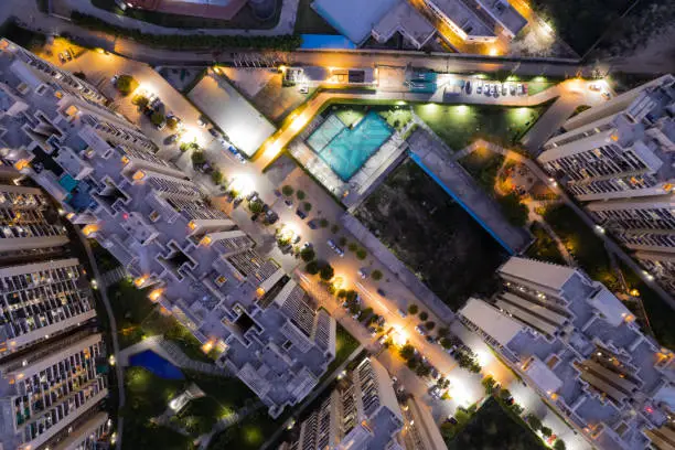 Photo of aerial drone shot ooking down over skyscrapers of a premium apartment complex with parking swimming pools with lights switched on at dusk twilight in gurgaon haryana India