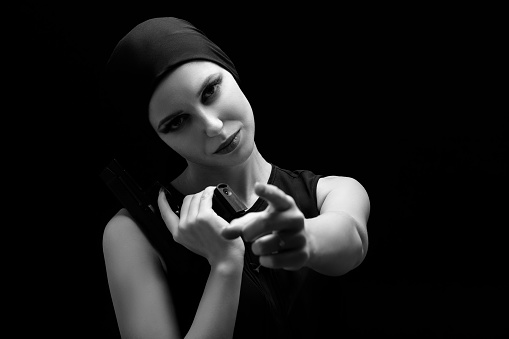 serious girl with gun point at camera on black background, monochrome