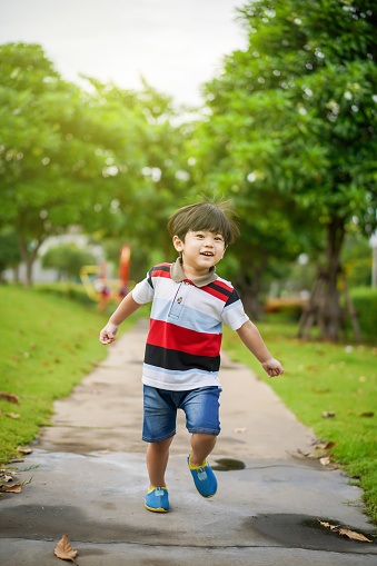 Playful Asian young boy playing and relaxing at the playground, innocence boy portrait. Cute Asian boy looking and smile at the camera for photograph with a beautiful nature bokeh background.