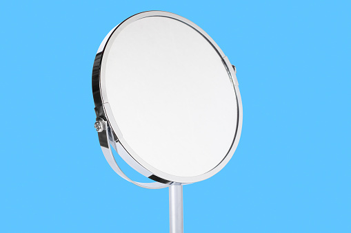 Desktop make up cosmetic mirror isolated on blue background. Home metal mirror close up isolated. Facial mirror