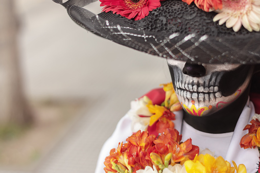 High angle view of a woman wearing La Calavera Catrina make-up and costume with her hat covering her eyes outdoors.