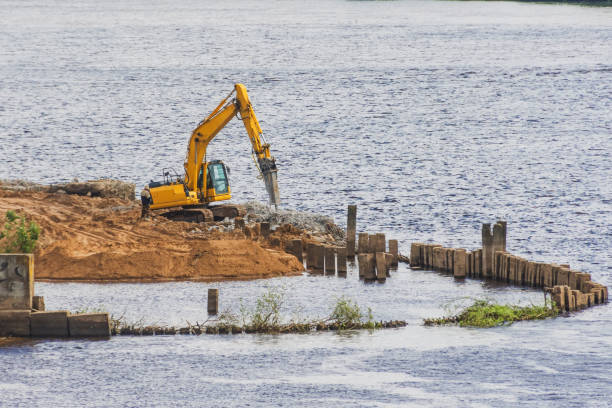 istock Excavator on the river bank with a jackhammer nozzle, embankment improvement work. 1414273581