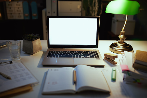 table with laptop, notebook and lamp at night in the modern office.