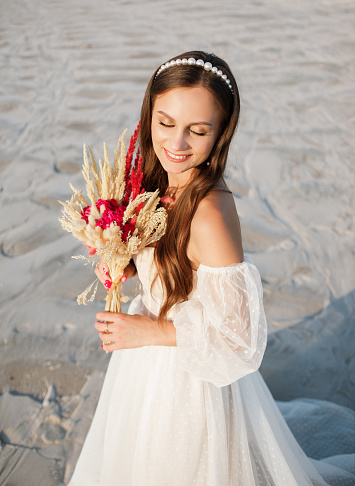Beautiful girl in wedding dress posing in front of desert, sand, canyon with a bouquet in her hands