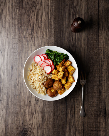 Homemade fried spicy tofu, grilled chestnut mushroom, radish pickles and poached spinach serves with boiled brown rice in a bowl.