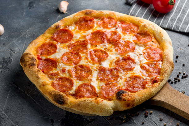 istock Pepperoni pizza on wooden board on grey table side view 1414281698