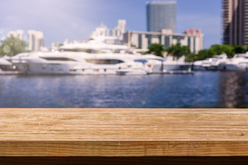 Summer background. Empty rustic wooden table with defocused sea, yachts and palm trees at background. Backdrop for product display on top of the table. Focus on foreground.