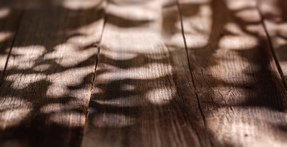Close-up of empty old wooden table with shadow of trees. Wooden background for product display on top of the table.