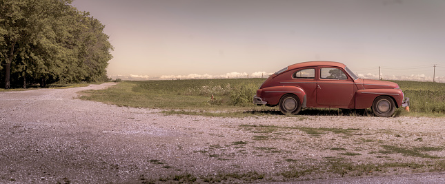 A vintage car on the side of an unpaved rural road