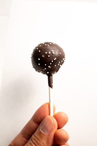 Hand holding a Chocolate Cake Pop with sprinkles on white