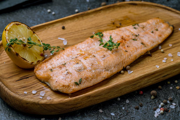istock Salmon steak on the grill on board on dark stone table macro close up 1414282895
